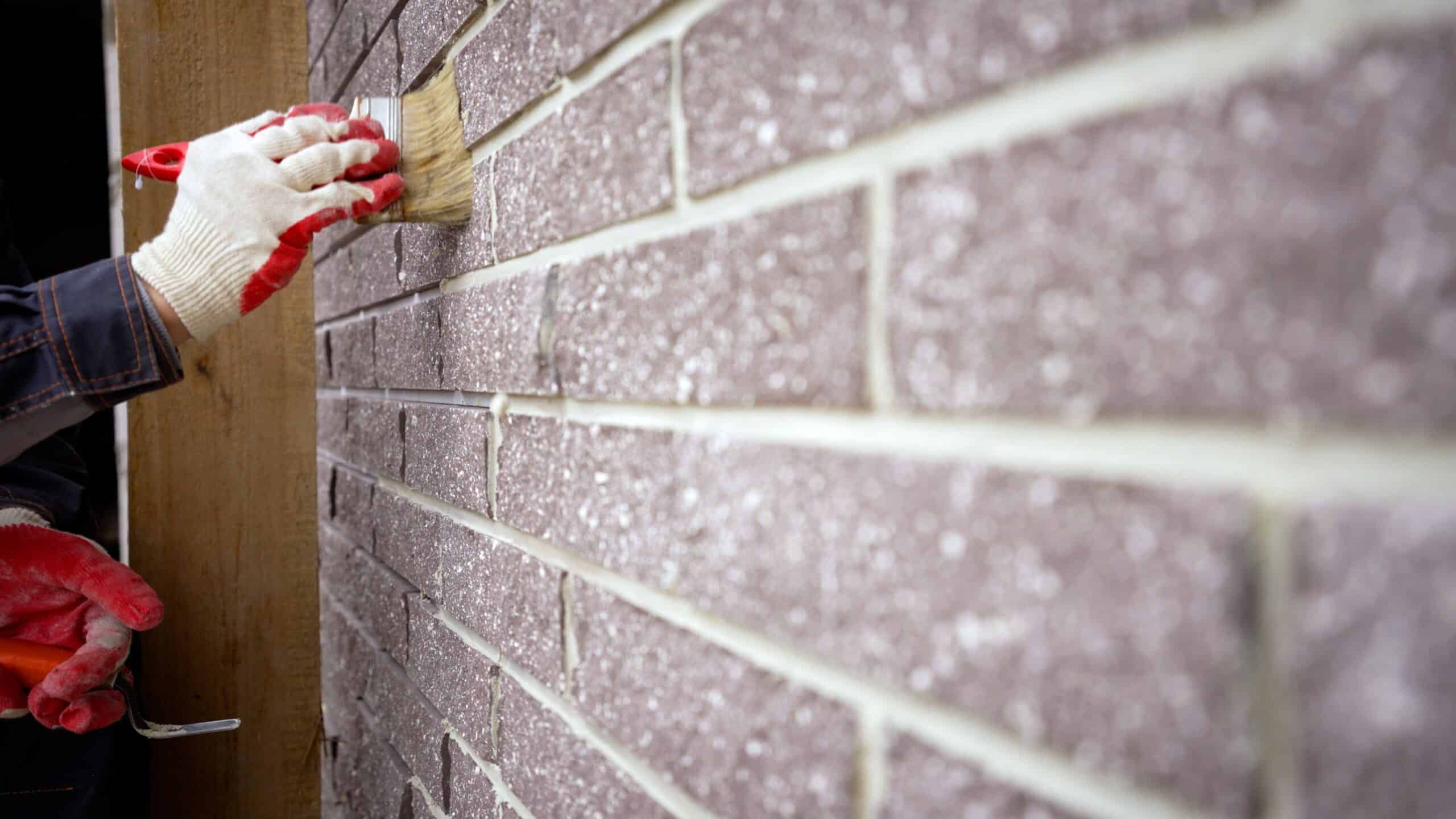Brush clean the facade of the house. Grouting the facade of the house. The worker with a brush cleans the tiles from the remnants of the solution on the facade of the house.